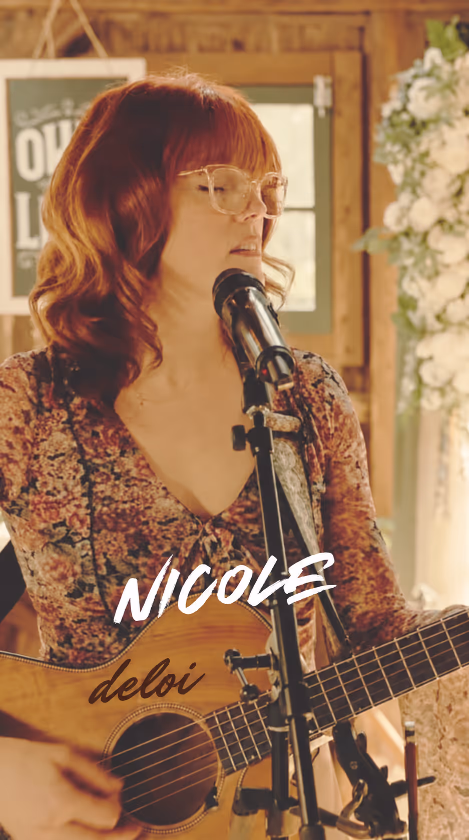 Nicole DeLoi singing and playing acoustic guitar, with her name overlaid on the photo